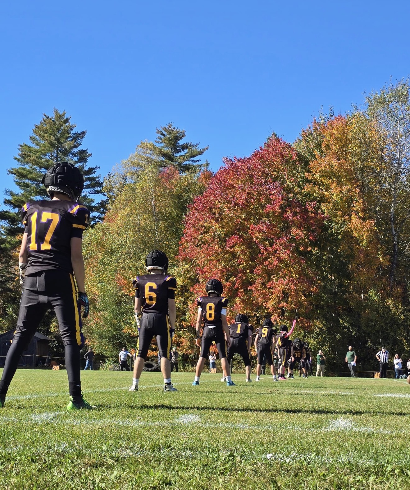 Mascoma Royals football players lined up on the field in front of colorful autumn trees